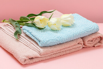 Stack of soft terry towels with tulips on a pink background.