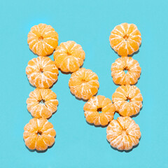 Creative layout of the letter N from peeled tangerines on a blue background. Flatlay.