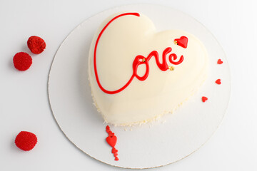 A cake in heart shape.  Mousse light cake in the shape of a heart with the inscription love with candy on a gray background. Valentine's Day.