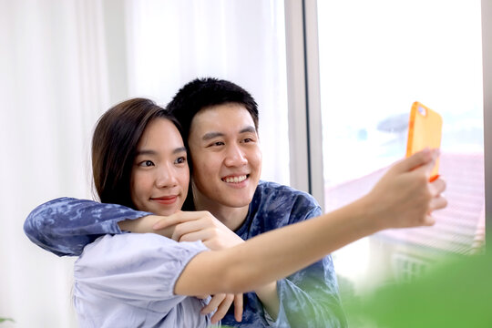 Asian couple making a selfie at hotel room by smartphone. Asian couples taking selfies at resort room. Journey, Travel concept. Honeymoon trip