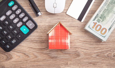 Wooden house model with a credit card, calculator, money, pen.