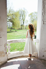 Fototapeta premium A woman with long red hair. A woman in a white dress stands on the porch. Beautiful hairstyle of long hair.