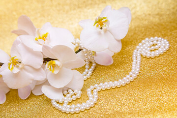 white Orchid and pearl necklace on a shiny gold background
