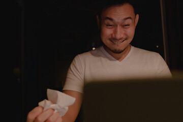 Funny horny face of Asian man watching porn at night.