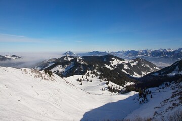 Fototapeta na wymiar Winterlandschaft der schneebedeckten bayerischen Alpen über Wolken vor blauem Himmel