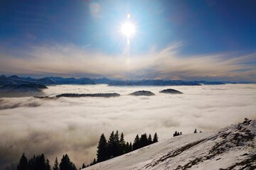 Winterlandschaft der schneebedeckten  bayerischen Alpen über Wolken vor blauem Himmel