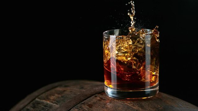 Ice dropped into glass of whisky on barrel in super slow motion. Shot with high speed cinema camera, 1000fps.