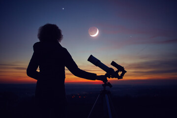 Woman looking at night sky with amateur astronomical telescope.