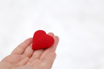 Red knitted heart in female palm of hand against the white snow. Concept of a romantic love, Valentine's day or charity