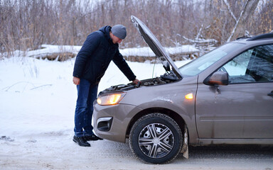 car repair on the road in winter. a young man is trying to fix a car breakdown under the soot on the road. woodsroadside assistance car.