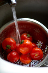 Fresh red tomatoes splashing in water before cooking at home, washes in a metal sink in the kitchen