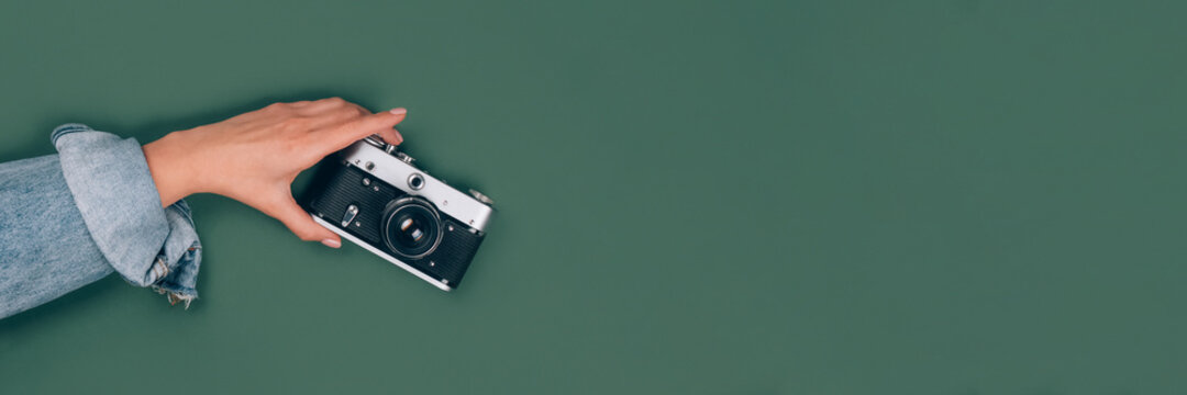 Banner with female hand holding old retro photo camera on green background with copy space for text. Trendy vintage photography, Online photography school concept, selective focus