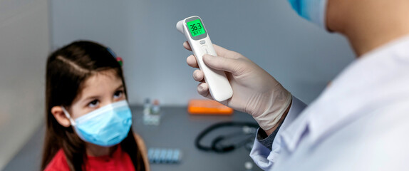 Female doctor looking at infrared thermometer after taking temperature of girl who has no fever