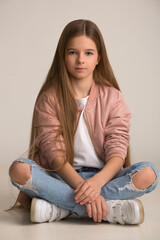 Fototapeta premium beautiful child girl with long hair in torn jeans on her knees and a pink leather jacket posing sitting