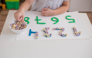 Child practice motor skills, make a numbers with play dough. Home education.