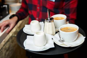 The waiter carries coffee, cream and sugar on a tray. Close-up, selective focus