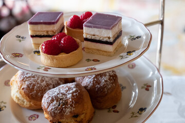 A selection of fine cakes and sandwiches on a cake stand as part of an English afternoon tea in a stately home.