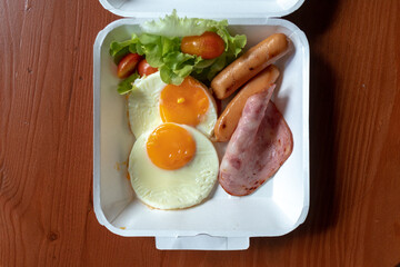 American breakfast meal style in a paper box set. Small meal of hams and fried eggs.