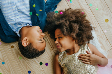 Two happy boy and girl lying on the floor under flying confetti