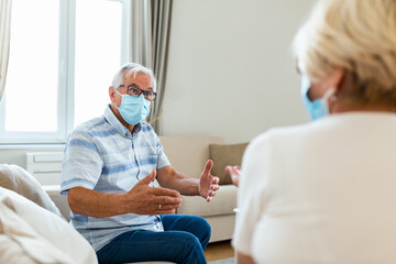 Fototapeta premium Old friends separated by social distancing on sofa at home. Senior friends wearing protective mask
