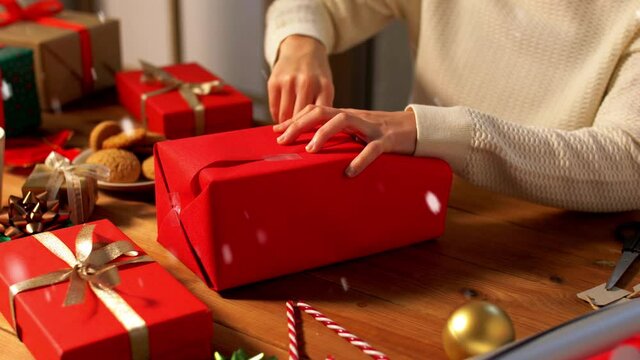 holidays, new year and christmas concept - woman wrapping gift box into red paper at home over snow