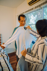 Asian senior couple fitting clothes in bedroom.