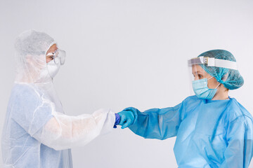 Young doctors greet fists in protective clothing on gray background. Pandemic greeting, social distance concept.