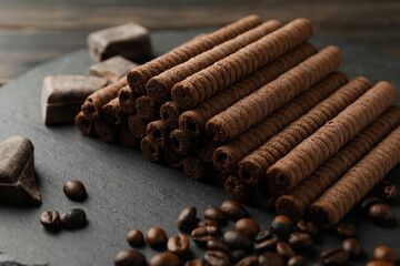 Tray with chocolate wafer rolls, coffee beans and chocolate on wooden background