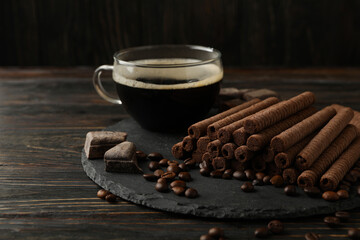 Concept of breakfast with coffee and chocolate wafer rolls on wooden background