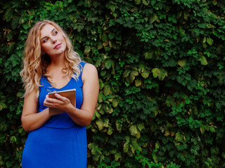 Young beautiful girl on a background of a wall of wild grapes, makes notes in a notebook, an idea has come. Copy space.