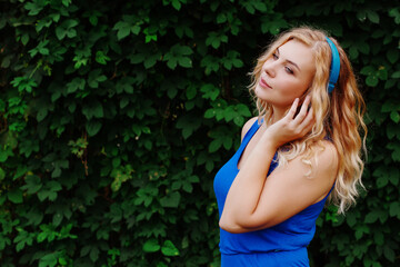 Beautiful young blonde girl in a dress listening to music in blue headphones. Real life, enjoy the moments. Copy space.