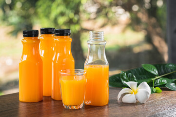 Fresh orange juice in no label clear plastic bottle with black cap on wooden table, natural trees blur in the background. With copy space.