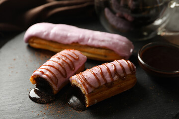 Tasty eclairs with delicious topping on black tray, close up