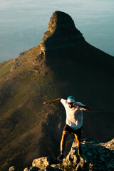 A young fit trail runner jumping across a steep ridge high in the mountains above Cape Town at sunset - 403396574