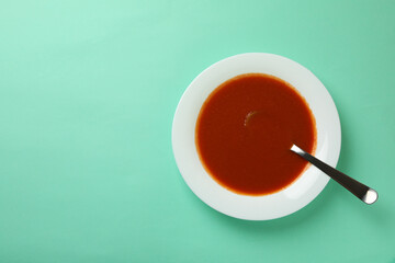 Plate of tasty tomato soup and spoon on mint background