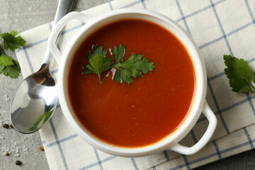 Bowl of tomato soup, spoon and towel on gray background