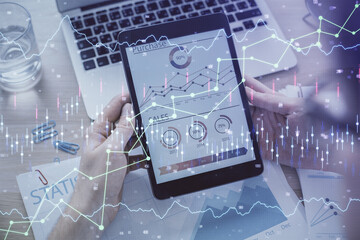 Double exposure of man's hands holding and using a digital device and forex graph drawing. Financial market concept.