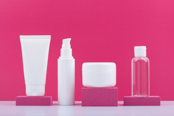 Set of cosmetic products in unbranded glossy white jars on pink podiums against bright pink background. Concept of beauty routine and skincare or anti aging treatment