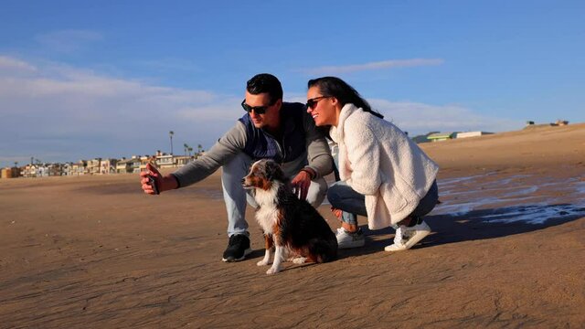 Happy couple taking a selfie with their dog on the beach