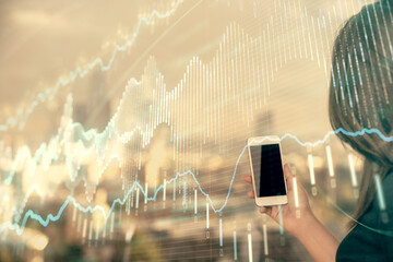 Double exposure of forex chart sketch hologram and woman holding and using a mobile device. Stock market concept.