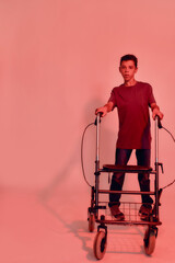 Full length shot of teenaged disabled boy with cerebral palsy looking at camera, taking steps with...