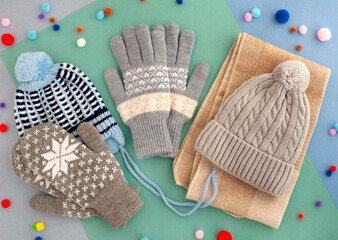 Hats and mittens for the cold season. Two hats, gloves and mittens on a colorful background. Clothes for autumn and winter. Hats, mittens, gloves in gray and blue tones.