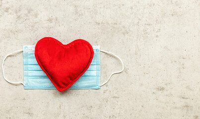 Red plush heart with face mask on concrete background. Top view, copy space. Valentine's day concept.