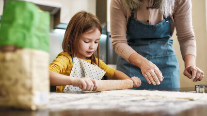 Little granddaughter rolling dough during home baking