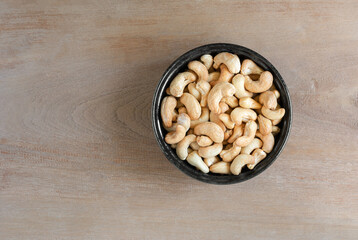 top view of homemade style roasted cashew nuts in a ceramic bowl on wooden table.