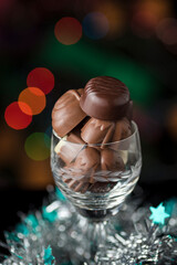 Vertical shot of chocolate candies in a glass and a Christmas decoration on a bokeh background