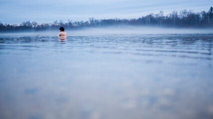 Fototapeta na wymiar Man taking an ice bath in a lake. Forrest in the winter haze. Cold water and low temperature.