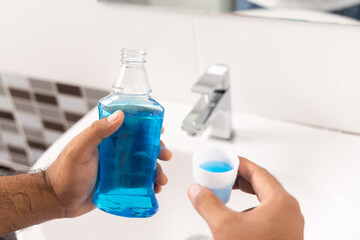 Young man is gargling with a blue mouthwash. For good dental health and fresh bad breath