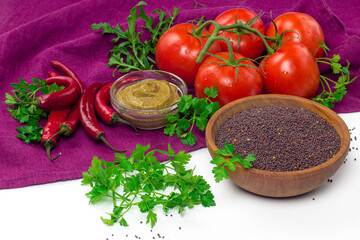 Black mustard seeds in wooden bowl and fresh vegetables. Mustard grain, tomatoes, red chili pepper,...