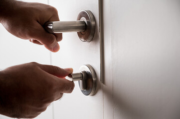A man's hand was grasping the handle to open the door. He unlocked the door to enter the room.